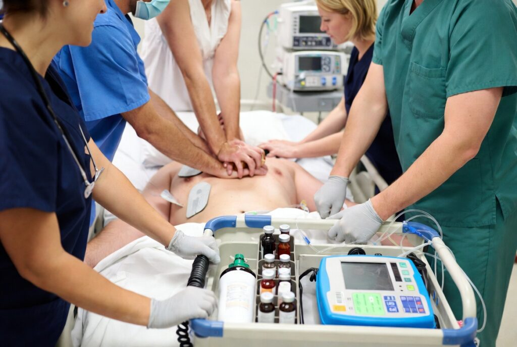 Equipe médica realizando RCP adulto com medicamentos de emergência no carrinho de parada